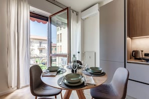 A dining area with a table set for two, a view of the outside, and a kitchen area with a kettle and a coffee maker. - Otium Lake Como (Como)