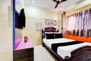 A bedroom with a bed, a vanity with a mirror, a ceiling fan, and a window with curtains. - Hotel O Manali Crossway Chennai (Chennai)