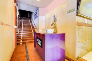 A hotel reception area with a staircase leading to the upper floors, a reception desk, and a wall-mounted sign indicating the reception. - Hotel O Manali Crossway Chennai (Chennai)