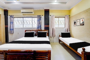 A hotel room with two beds, a window with metal bars, and an air conditioning unit.