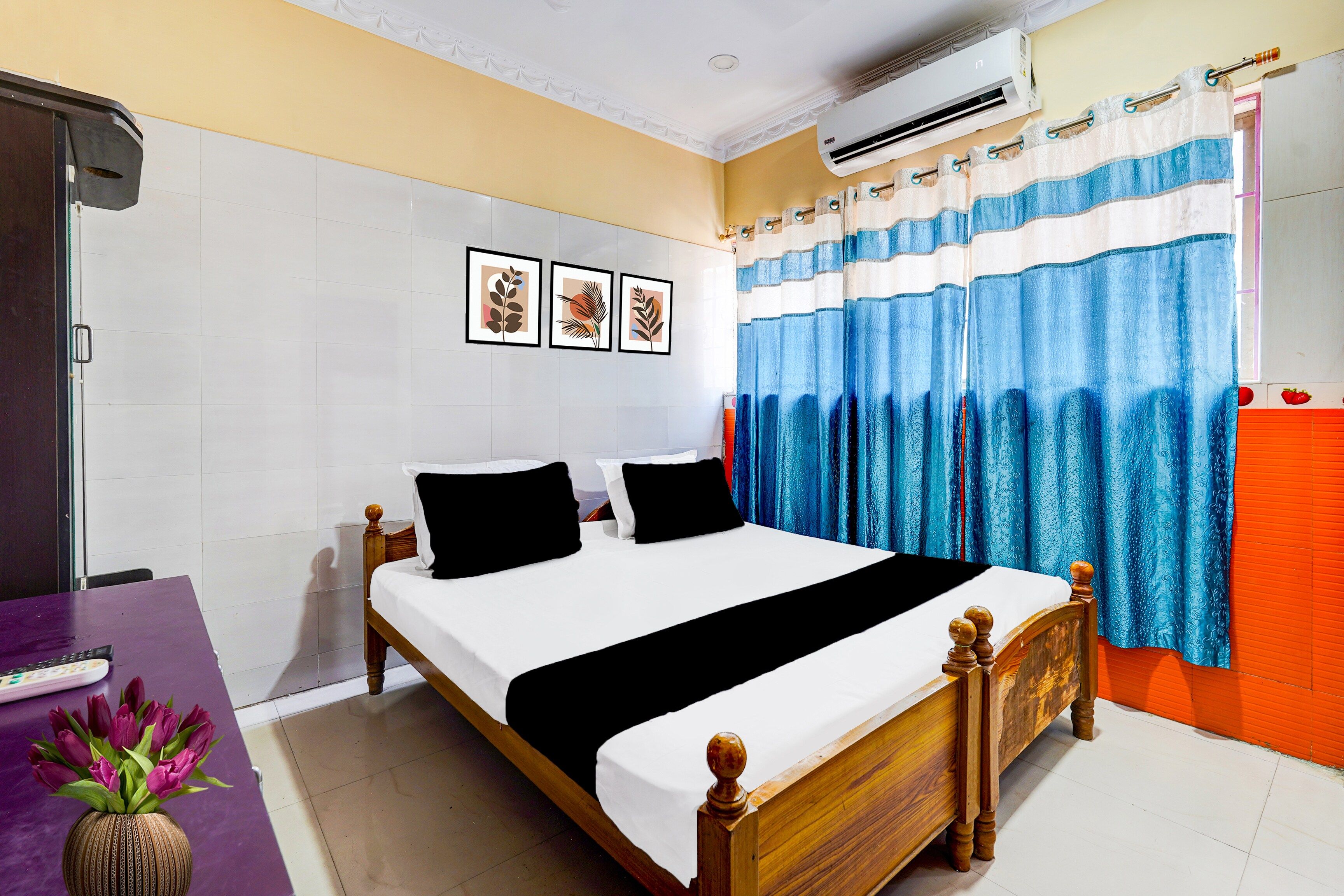 A hotel room with a bed, a desk, a chair, a vase of flowers, and a window with curtains.