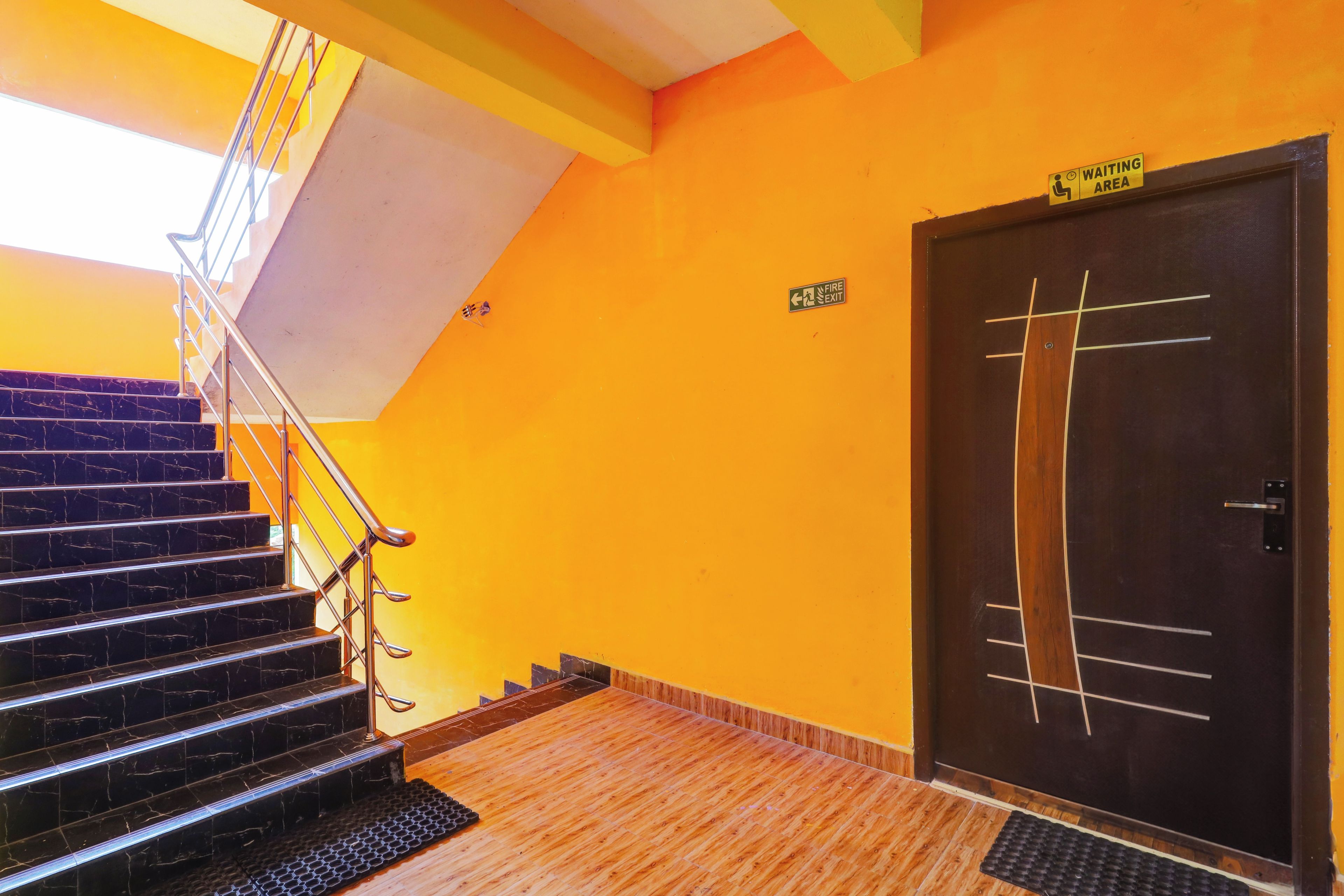 Un escalier menant à une porte signalée comme étant une issue de secours, ainsi qu’un panneau indiquant une zone d’attente accessible aux personnes à mobilité réduite et un autre panneau indiquant une issue de secours sur le mur.