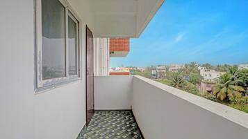 Un balcón con suelo de baldosas, una ventana y vistas a una zona residencial con edificios y árboles.