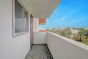 A balcony with a tiled floor, a window, and a view of a residential area with buildings and trees.