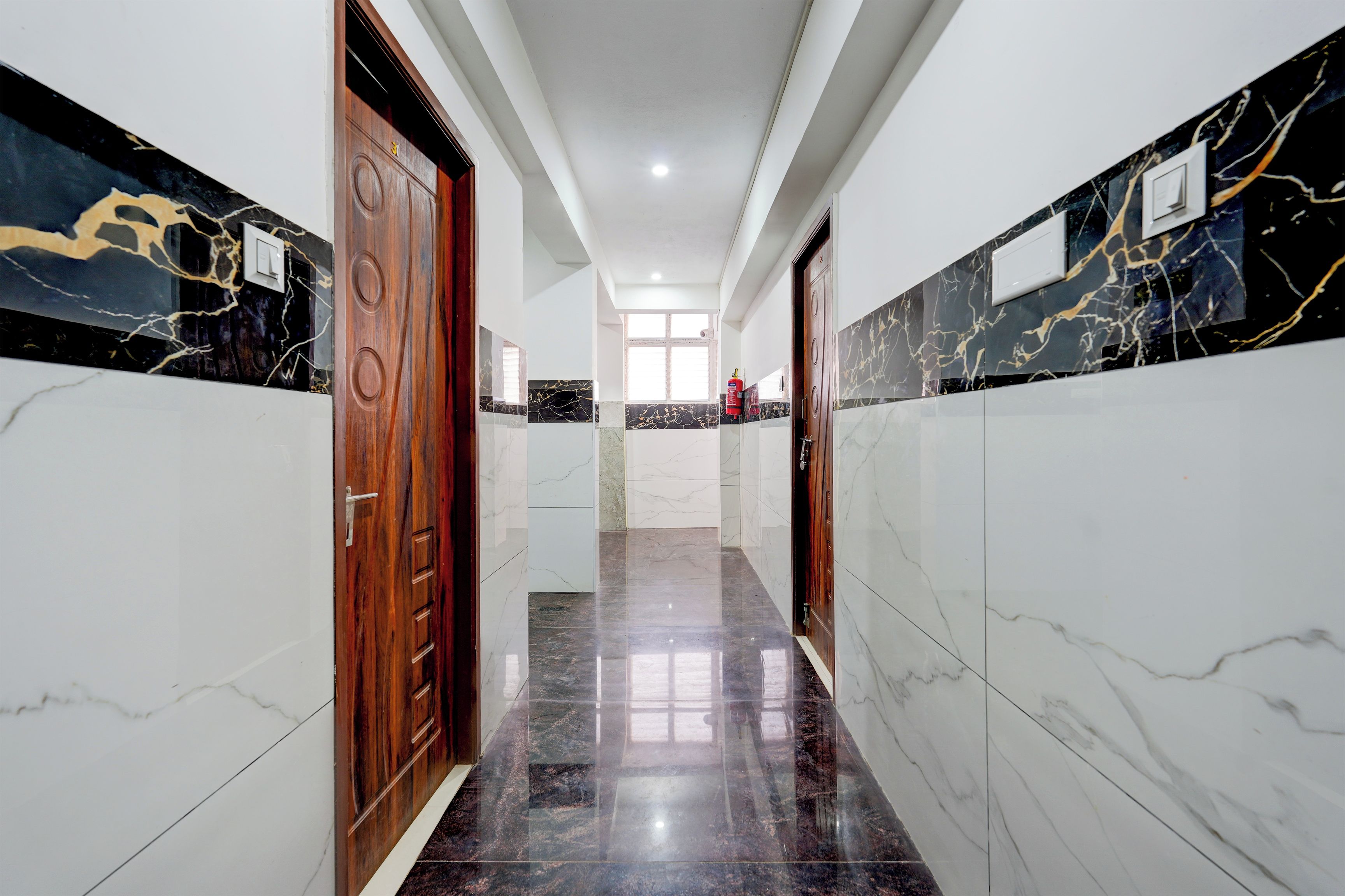 A hallway with marble flooring, wooden doors, and a fire extinguisher mounted on the wall.