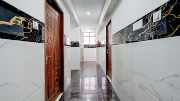 A hallway with marble flooring, wooden doors, and a fire extinguisher mounted on the wall.