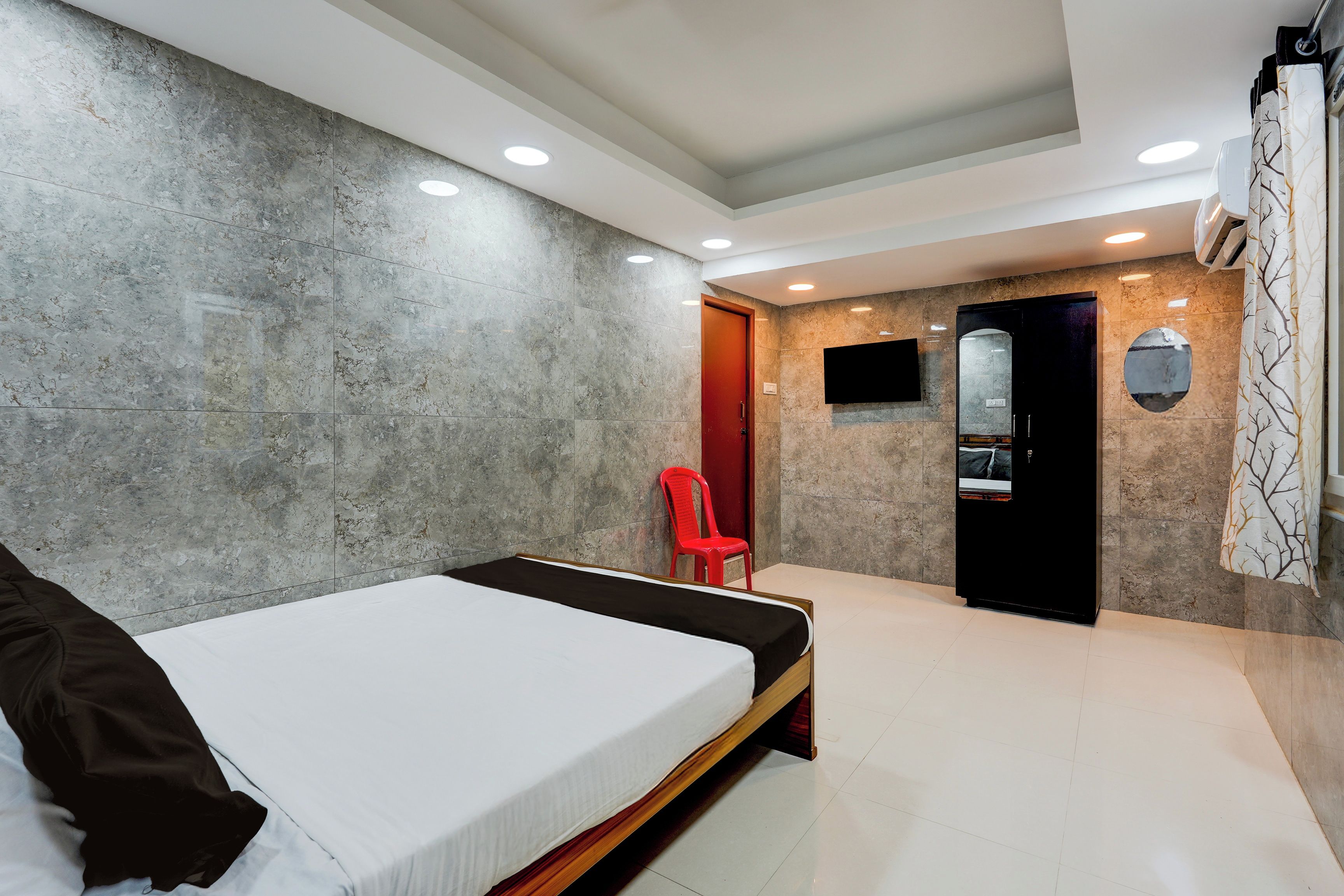 Un dormitorio moderno con una cama, una silla roja, un televisor y un espejo.