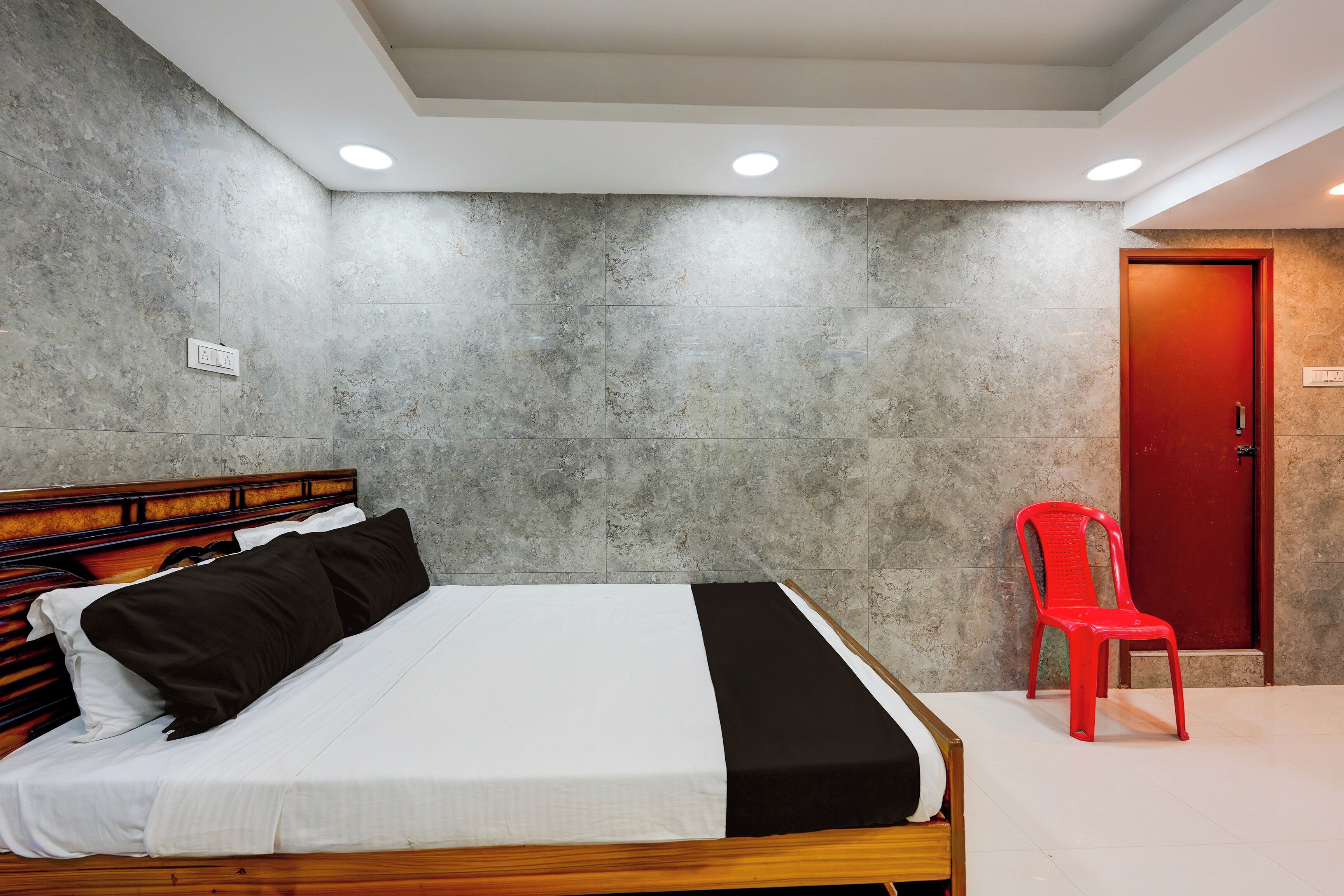 Ein Schlafzimmer mit einem Bett, einem hölzernen Kopfteil, einem roten Sessel und einer roten Tür.