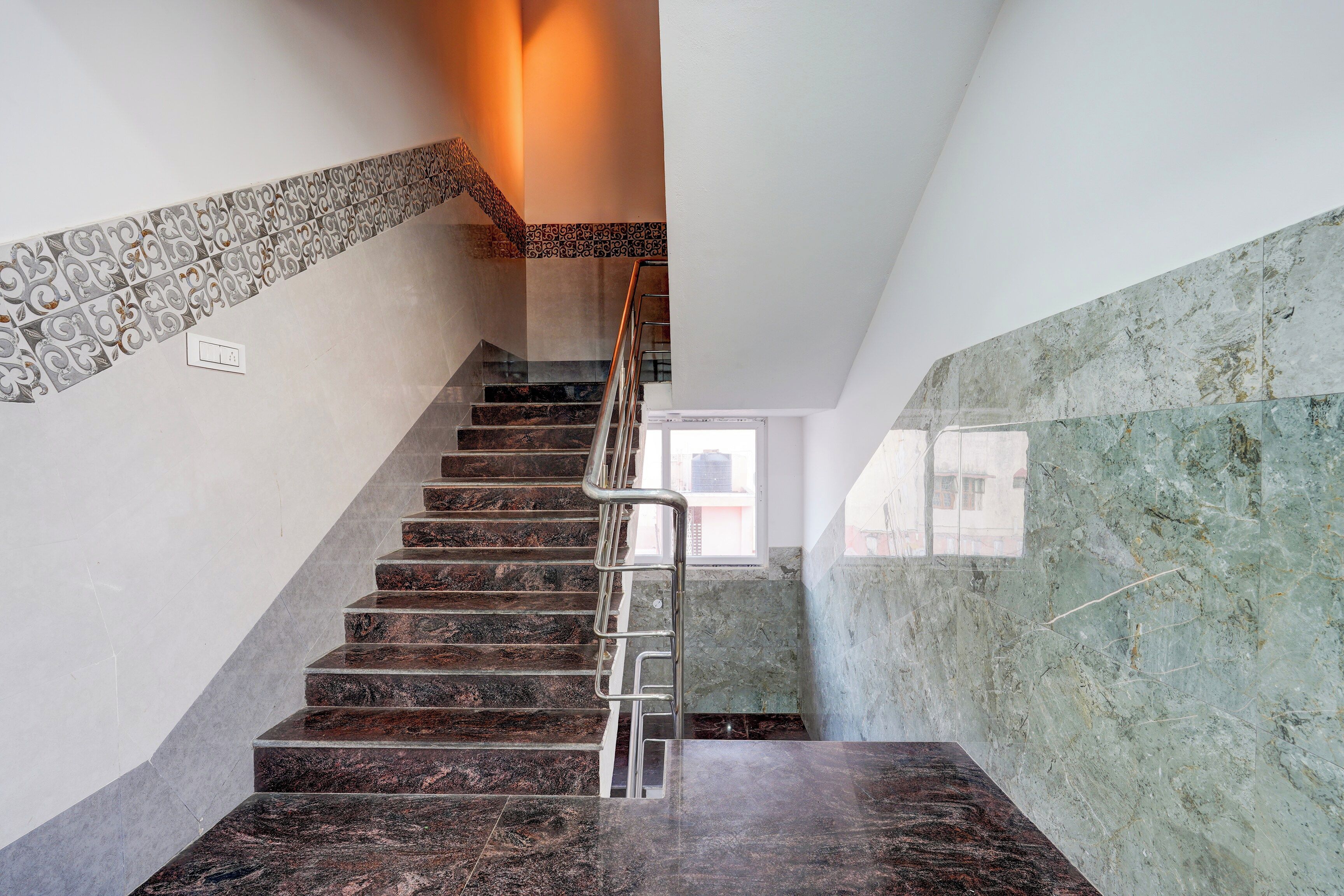 Una escalera con barandilla metálica, azulejos decorativos en la pared y un ventanal en la parte superior.