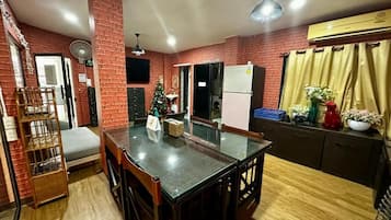 A dining area with a brick wall, a Christmas tree, a refrigerator, and a window with curtains.