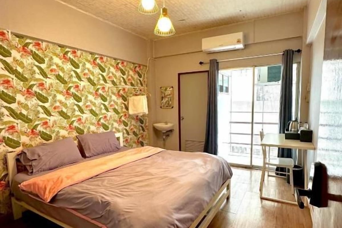 A bedroom with a bed, wooden flooring, a window, and a door.