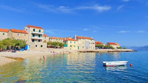 Uma vila costeira com edifícios de pedra, águas cristalinas e um barco ancorado perto da praia.