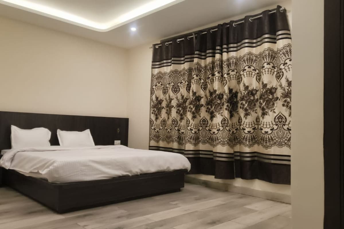 A modern bedroom with a dark headboard, a large bed with white bedding, and a patterned curtain.