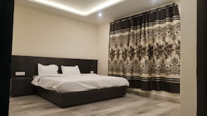 A modern bedroom with a dark headboard, a large bed with white bedding, and a patterned curtain. - Saima Luxury (Srinagar)