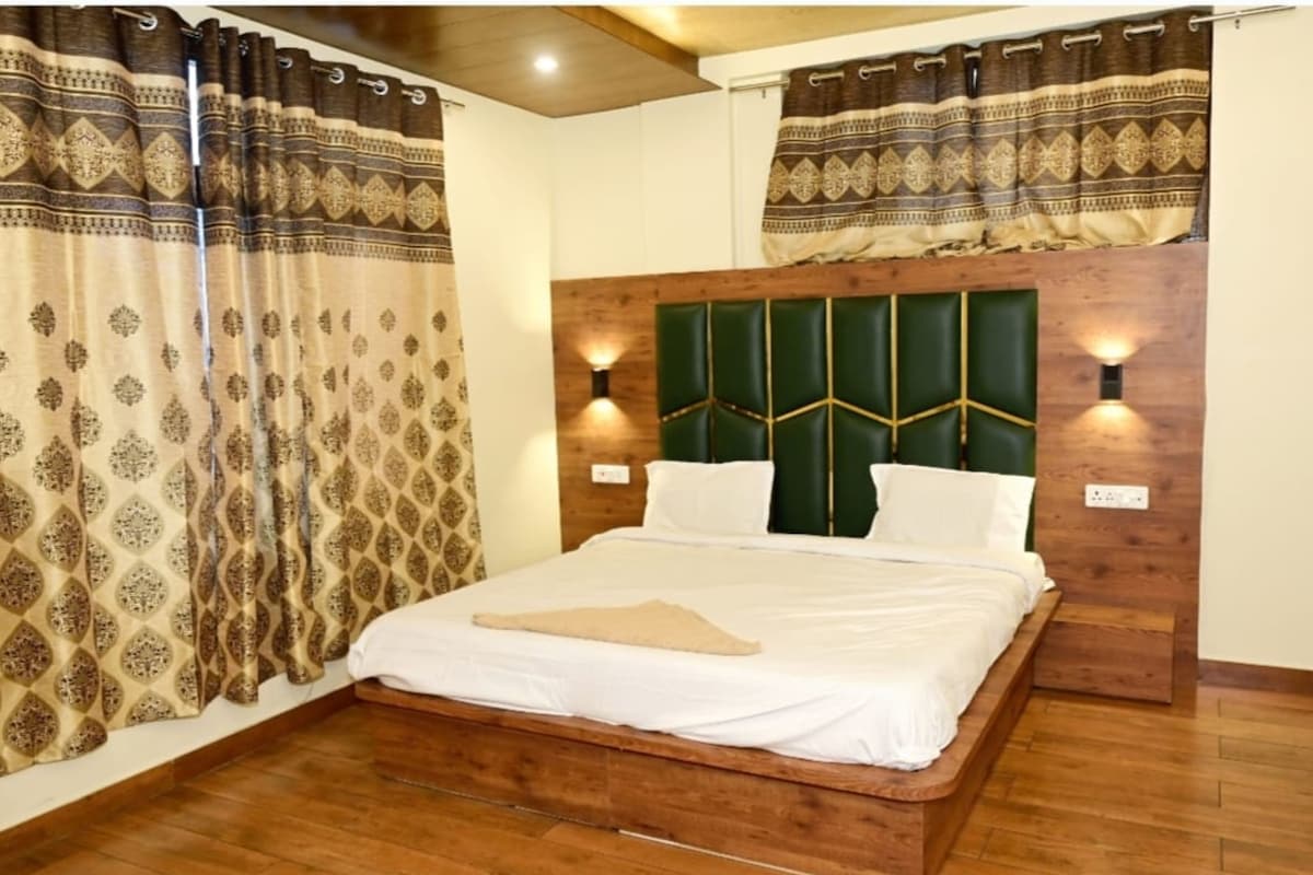 A bedroom with a wooden headboard, two bedside lamps, and patterned curtains.