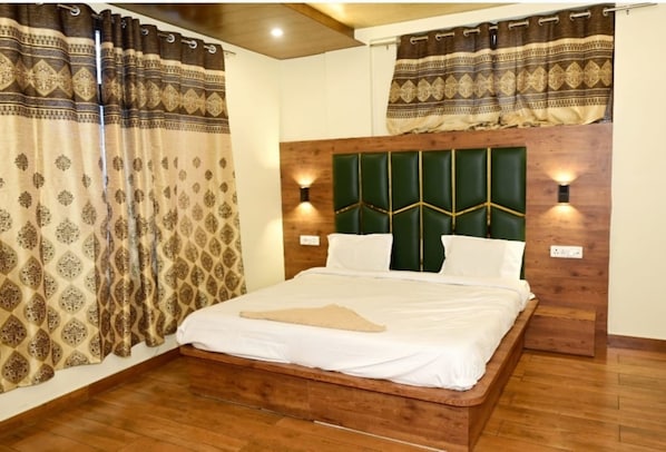 A bedroom with a wooden headboard, two bedside lamps, and patterned curtains. - Saima Luxury (Srinagar)