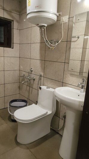 A bathroom with a toilet, bidet, sink, and a water heater mounted on the wall. - Saima Luxury (Srinagar)