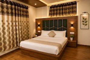 A hotel room with a large bed, wooden headboard, two wall-mounted lights, a potted plant, and patterned curtains. - Saima Luxury (Srinagar)