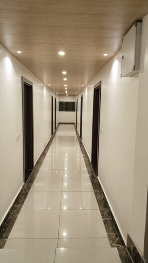 A long, narrow hallway with a shiny tiled floor and evenly spaced doors on both sides. - Saima Luxury (Srinagar)