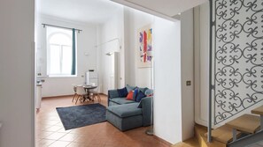A modern living room with a grey sofa, a dining table with chairs, and a large window with curtains. - Vittorio Elegant Two Bedroom Apartment (Roma)