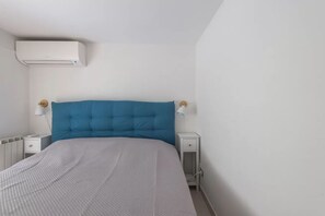 Ein Schlafzimmer mit einem Bett, weißen Nachttischen, einem blauen Kopfteil und einer Klimaanlage.