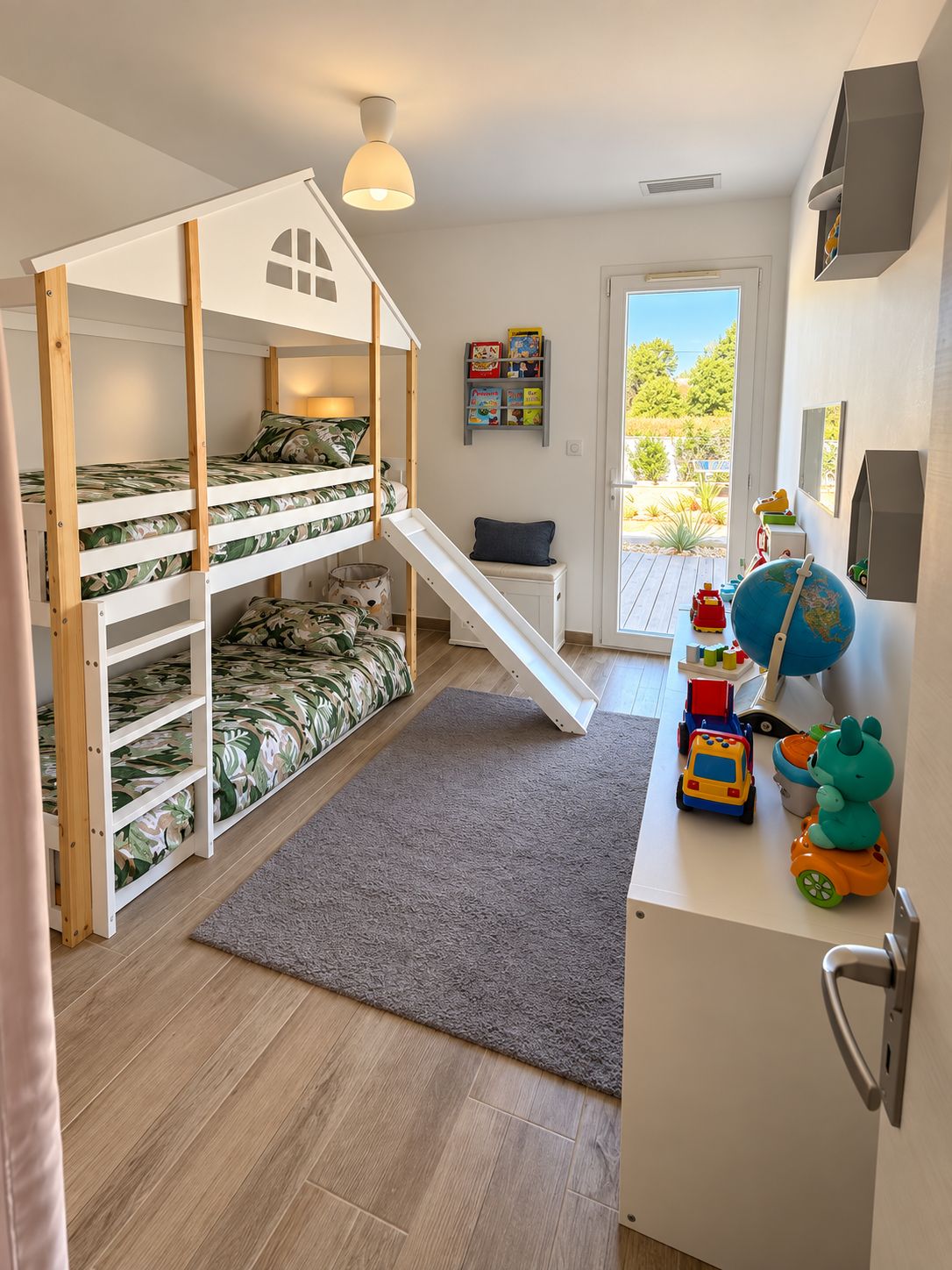 A children's room with bunk beds, a slide, a desk with toys, and a window with a view of greenery.