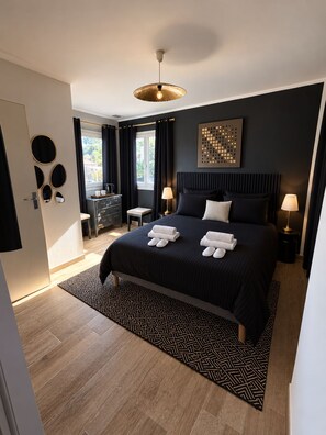 Ein modernes Hotelzimmer mit einem großen Bett, zwei Nachttischen, einem Schreibtisch und einem Fenster mit Vorhängen.