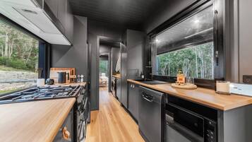 Une cuisine moderne avec un plan de travail en bois, des appareils électroménagers noirs et une vue sur l’extérieur.