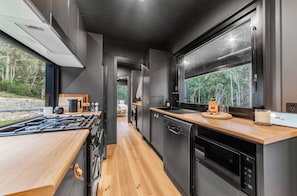 A modern kitchen with a wood countertop, black appliances, and a view of the outdoors.