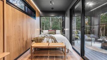 A modern bedroom with a bed, bench, and large windows.