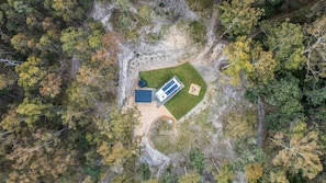 An aerial view of a property with a large building, a fenced area, and surrounding forest.