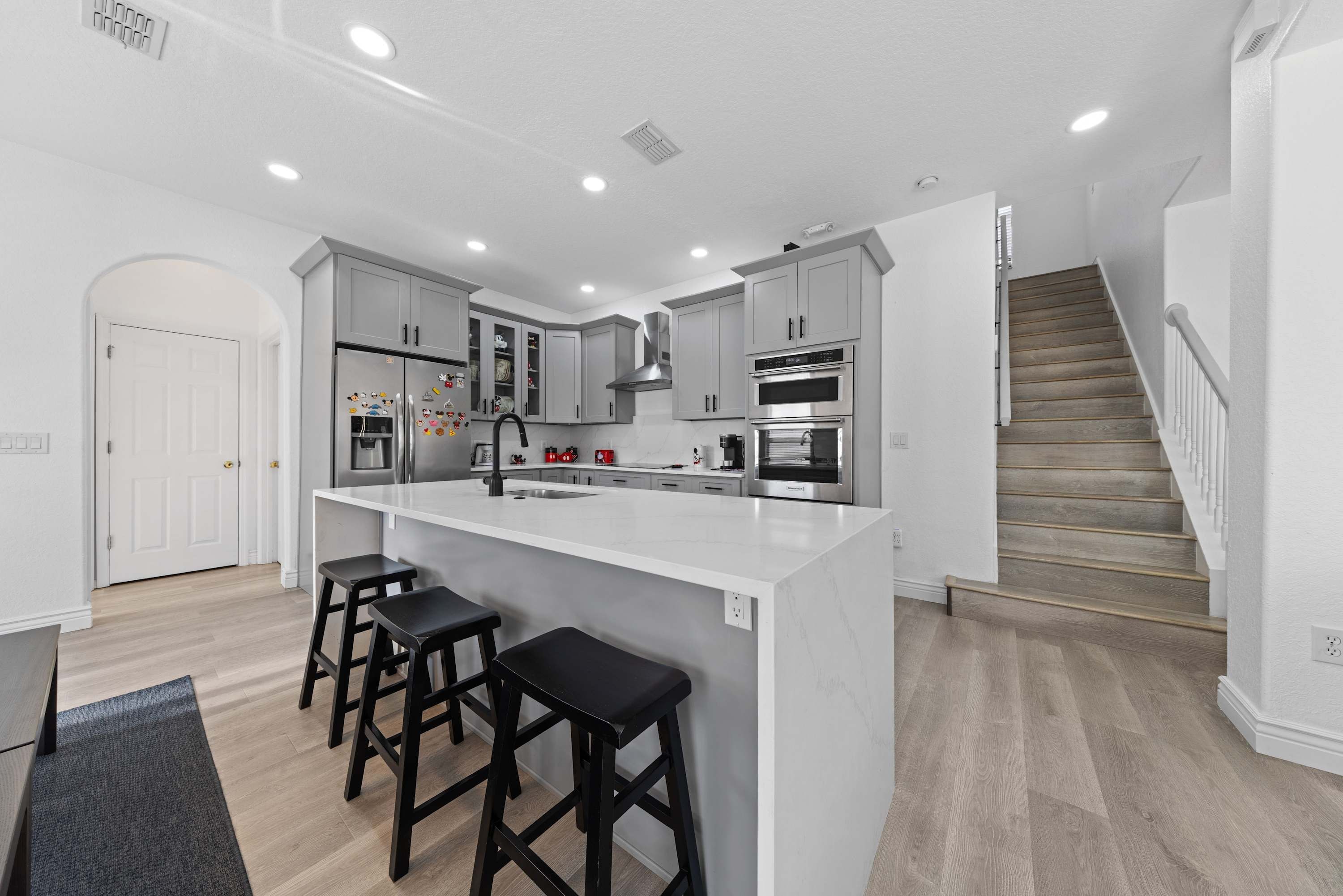 A modern kitchen with a central island, bar stools, and a staircase leading to another level.