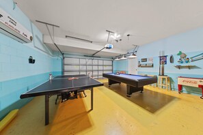 Ein Spielzimmer mit Tischtennisplatte, zwei Billardtischen und verschiedenen Annehmlichkeiten, darunter ein Coca-Cola-Kühler.