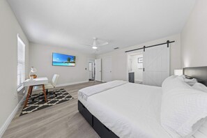 Ein Schlafzimmer mit einem Bett, einem Schreibtisch, einem Stuhl, einem Deckenventilator und einem Bild an der Wand.