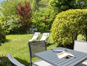 Eine Terrasse mit zwei Liegestühlen und einem Tisch, umgeben von üppiger Vegetation und Bäumen.
