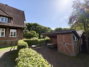 A brick house with a tiled roof, a small patio area with a table and benches, and a garden with hedges. - Großes Fachwerkhaus für 20 Personen bei Hannover, perfekt für Familien + Firmen (Langenhagen)