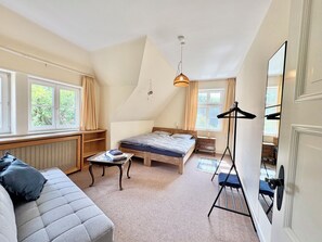 A bedroom with a bed, a sofa, a radiator, a hanging light fixture, and a window with curtains. - Großes Fachwerkhaus für 20 Personen bei Hannover, perfekt für Familien + Firmen (Langenhagen)