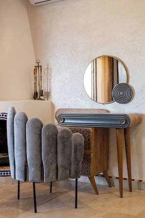 Ein Zimmer mit Kamin, einem runden Spiegel und einem modernen Stuhl mit Holzfüßen.