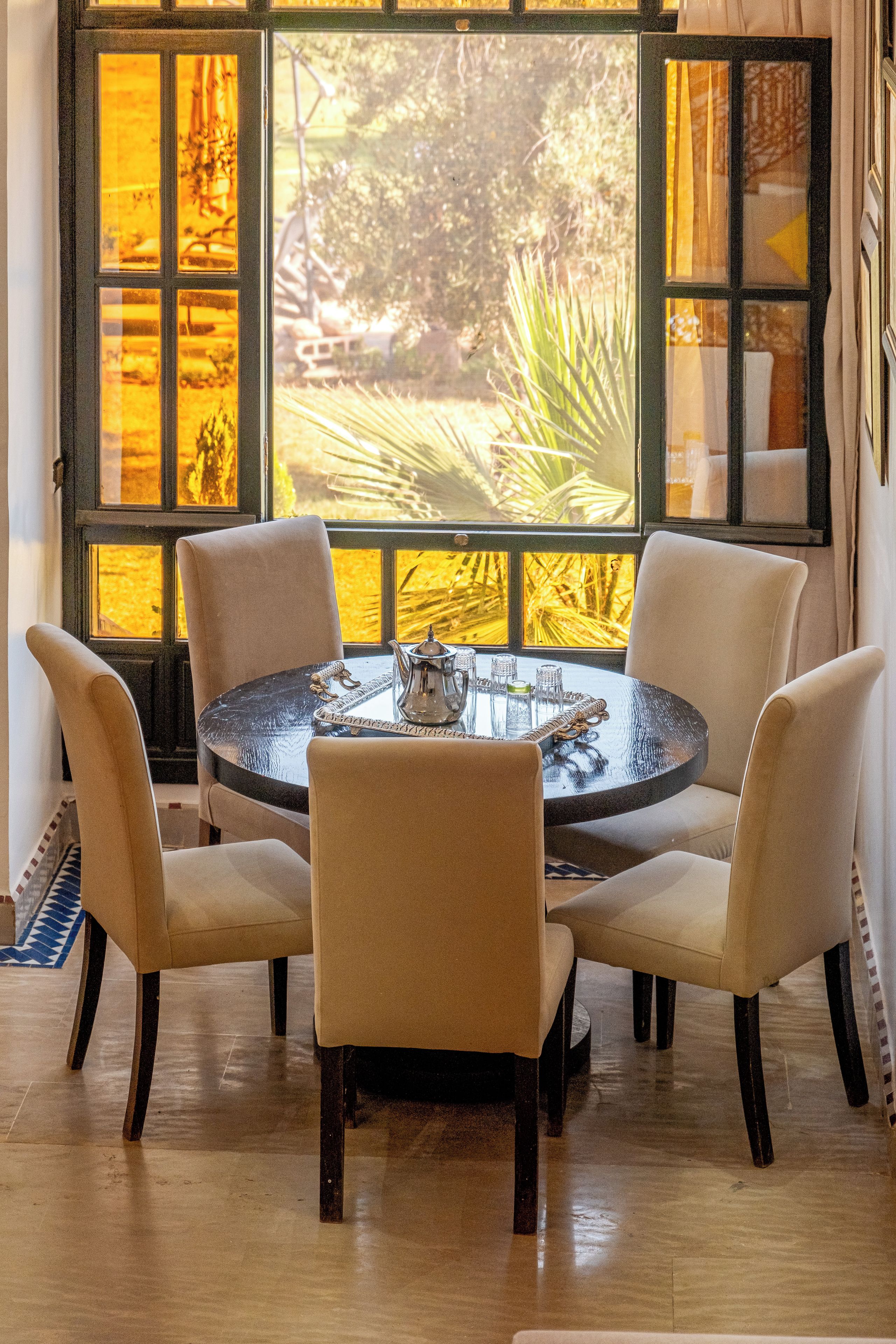 Una mesa redonda con cuatro sillas, una bandeja decorativa y vistas a zonas verdes a través de amplios ventanales.