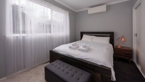 Un dormitorio con una cama, una mesita de noche, una lámpara y una ventana con cortinas translúcidas.