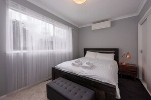 A bedroom with a bed, a bedside table, a lamp, and a window with sheer curtains. - Homely and Cozy 1BDR Unit in Leafy Hawthorn (Hawthorn)