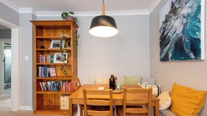 Un comedor con una mesa y sillas de madera, una estantería, una lámpara colgante y un cuadro en la pared.