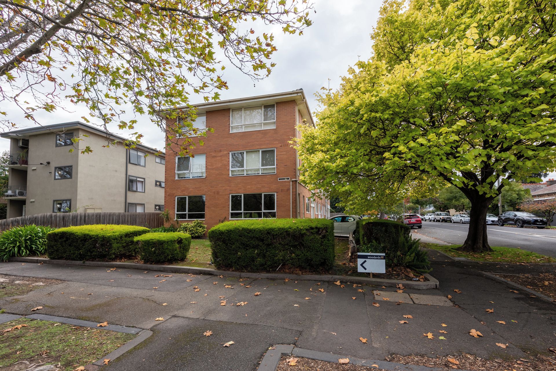 A multi-story residential building with a brick facade, a well-maintained lawn, and a street view with parked cars.