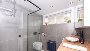 Un baño moderno con cabina de ducha de vidrio, inodoro, lavabo con encimera de madera y ventana con plantas.