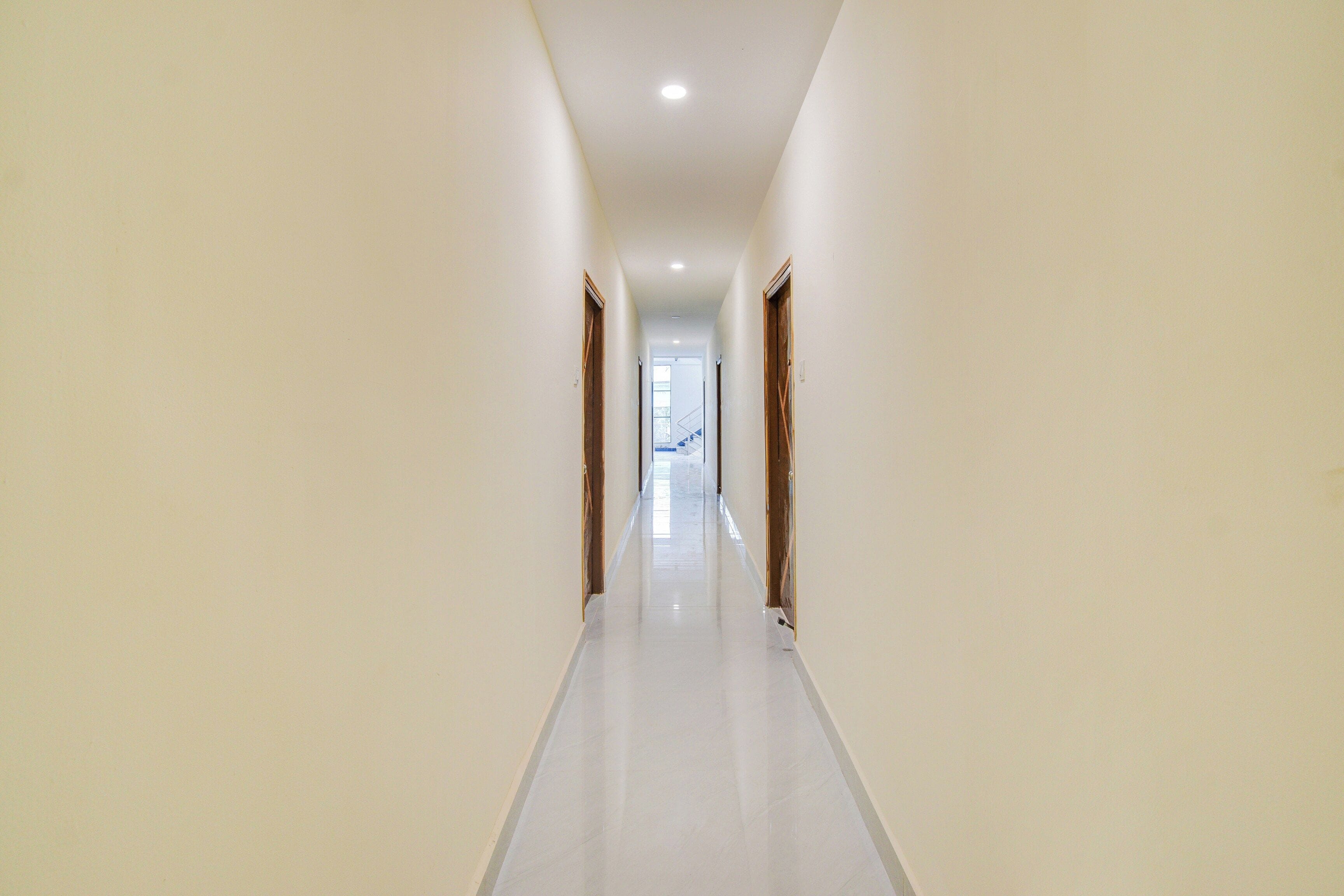 A long, narrow hallway with white walls and a shiny floor, leading to a staircase at the end.