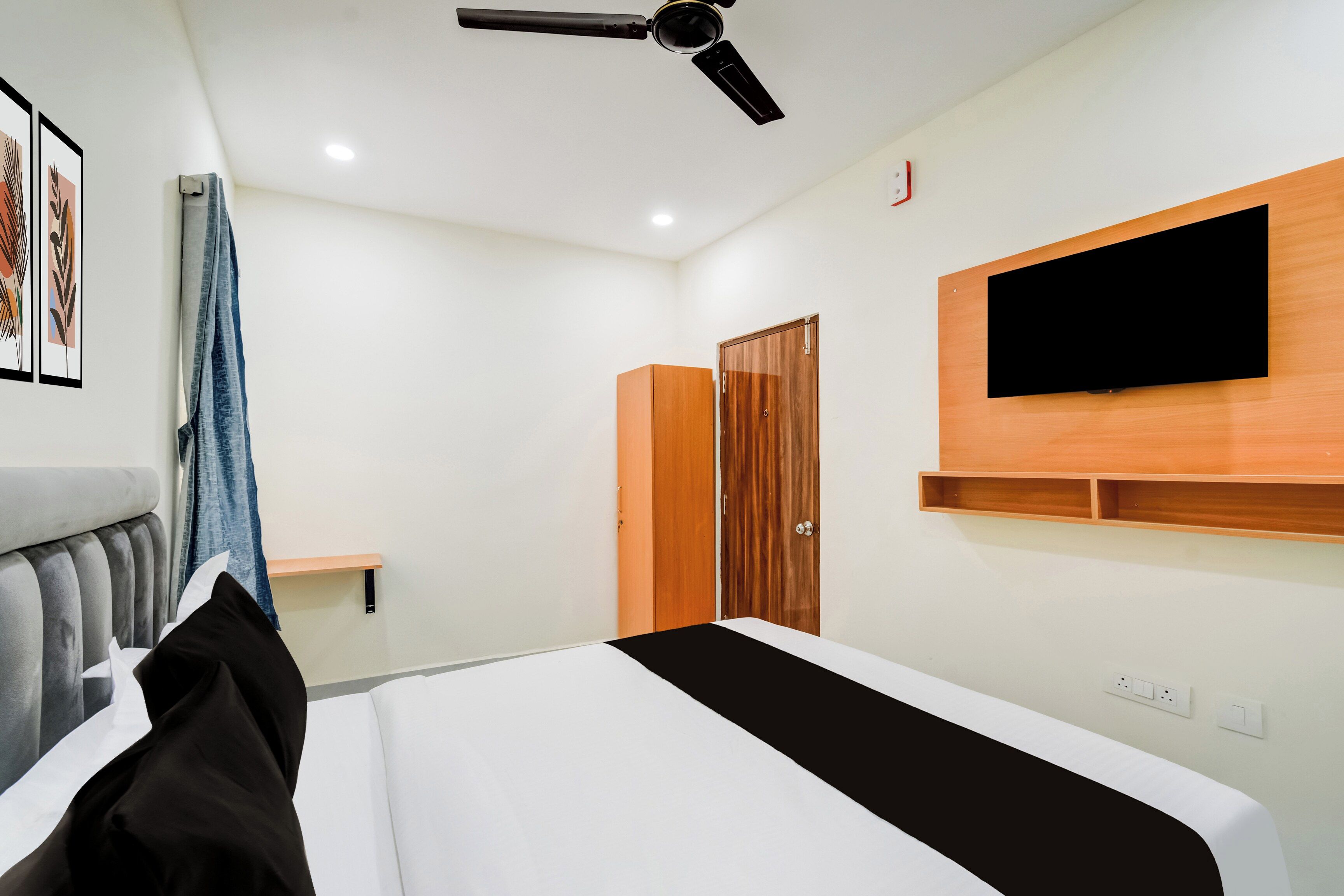A modern bedroom with a bed, a ceiling fan, a mounted TV, and a wardrobe.