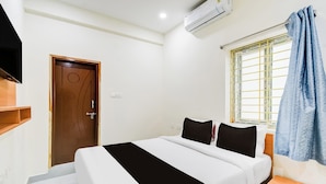 Een hotelkamer met een bed, een aan de muur bevestigde televisie, een airconditioningapparaat, een raam met gordijnen en een deur.