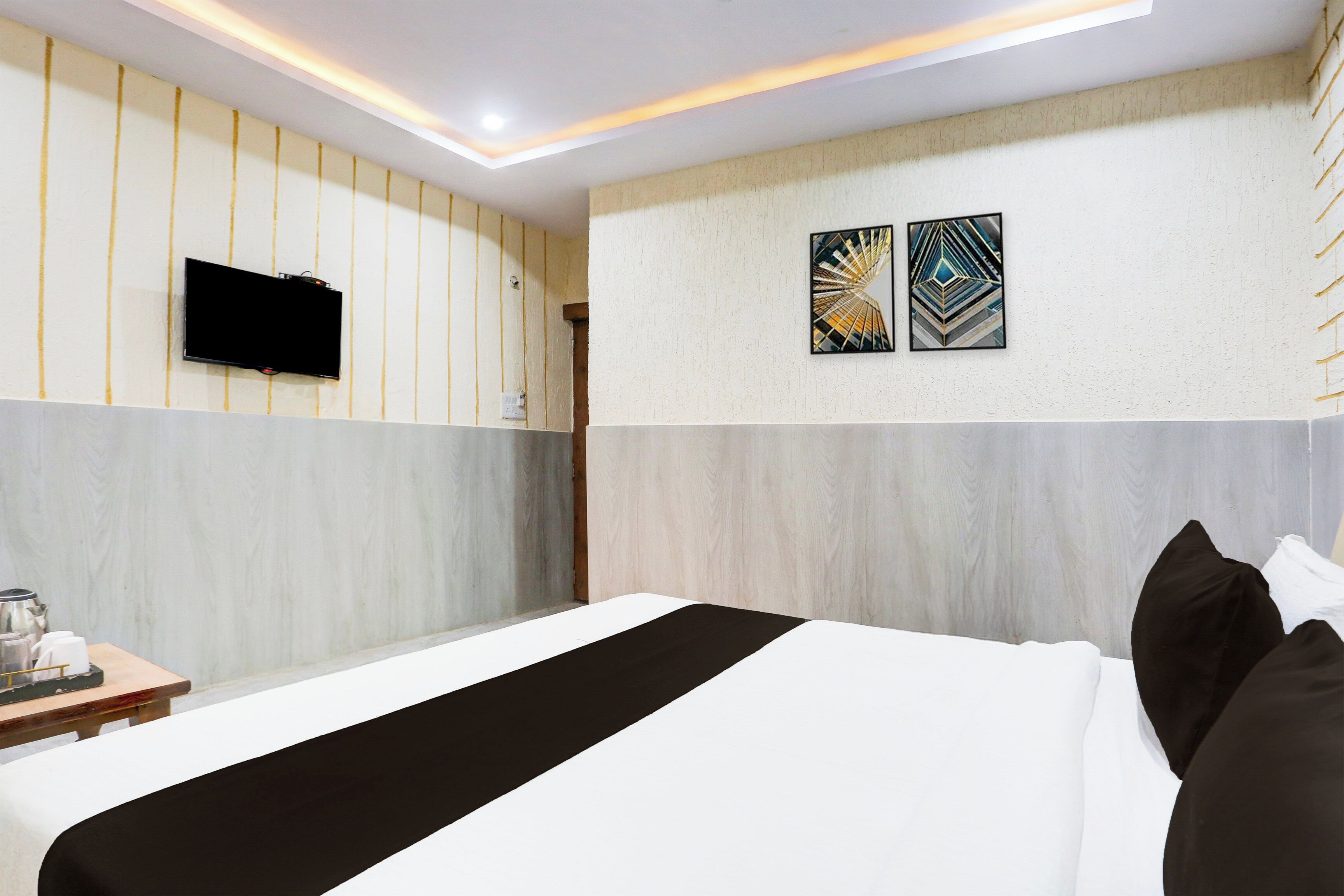 A hotel room with a bed, a flat-screen TV mounted on the wall, and two pieces of wall art.