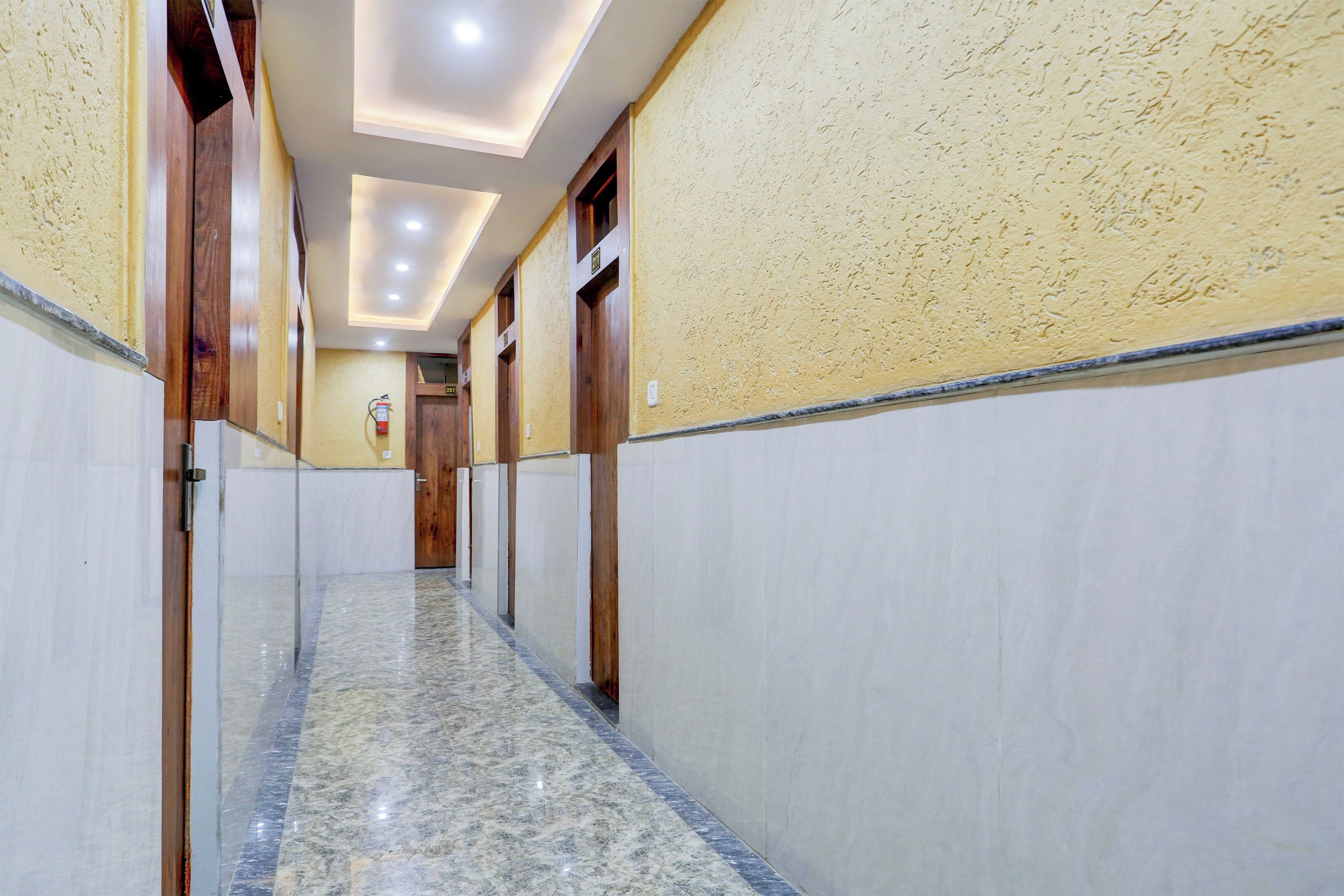 A hotel corridor with marble flooring, wooden doors, and a fire extinguisher on the wall.