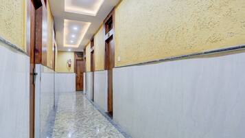 A hotel corridor with marble flooring, wooden doors, and a fire extinguisher on the wall.
